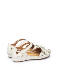 Sandales en cuir blanc avec design floral découpé, sangle ajustable et couture tissée le long de la semelle. Semelle plate et forme de tête ronde.
