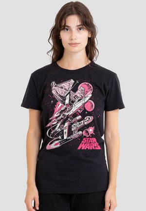 Young woman wearing black Star Wars t-shirt featuring pink and white spaceships and planets against a plain light gray background.