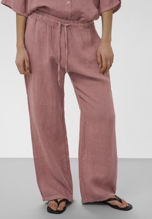 Pantalon large en lin rose avec taille élastique et cordon, associé à des tongs noires sur un sol gris.