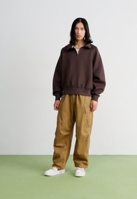 Brun pullover med dragkedja i kragen och ribbad nederkant, tillsammans med beigefärgade cargobyxor med sidofickor. Vita sneakers fulländar looken.