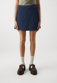 Denim omslagskjol i mörkblått med sidband. Matchad med ljusgrå knälånga strumpor och bruna skor med tjock sula.