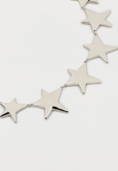 Strieborné kovové hviezdicové články prepojené do zakrivenej reťaze na obyčajnom bielom pozadí.