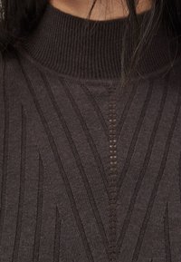 Dunkelbrauner gerippter Rollkragenpullover mit vertikaler Textur und einem mittigen Schlitzdetail. Das weiche Strickmaterial hat eine figurschmeichelnde Passform.