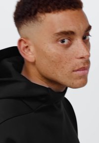 Felpa nera con cappuccio dal texture morbido e design minimalista, dotata di cordini regolabili e vestibilità ampia, indossata da un modello.