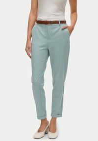 Pantaloni fitted in un verde teal chiaro con una superficie liscia, dotati di una cintura in pelle marrone. Le tasche frontali e i risvolti apportano dettagli funzionali.