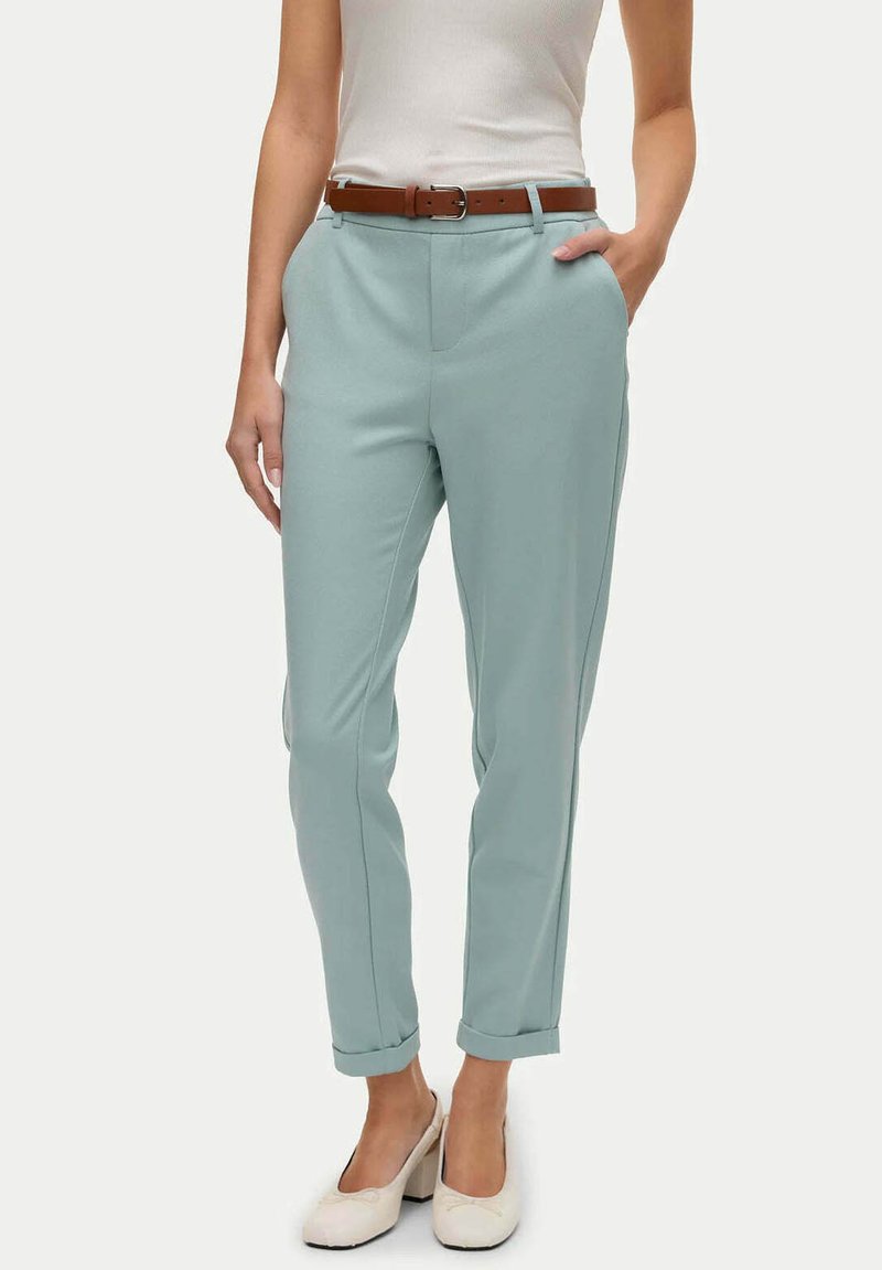 Pantaloni fitted in un verde teal chiaro con una superficie liscia, dotati di una cintura in pelle marrone. Le tasche frontali e i risvolti apportano dettagli funzionali.