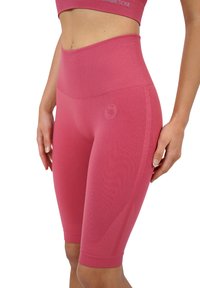 Pantaloni biker rosa a vita alta con texture liscia, design attillato e marchio sulla vita. Taglio fino al ginocchio senza chiusure visibili.