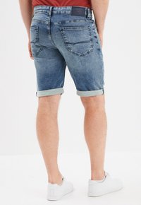 Pantalones cortos de denim en azul claro, con dobladillos enrollados, bolsillos traseros con detalles de costura y una banda de cintura con marca. Combinados con zapatillas blancas.