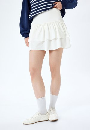 Witte gelaagde rok met een geribbelde tailleband, gemaakt van zachte stof. Gemaakt met een marineblauwe gestreepte sweatshirt, witte sneakers en enkelsokken.