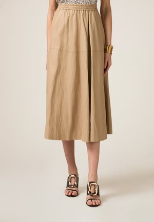 Falda beige de longitud media con cintura elástica, que presenta una textura suave y arrugada. Combinada con sandalias negras de tira decoradas con acentos de hardware dorado.
