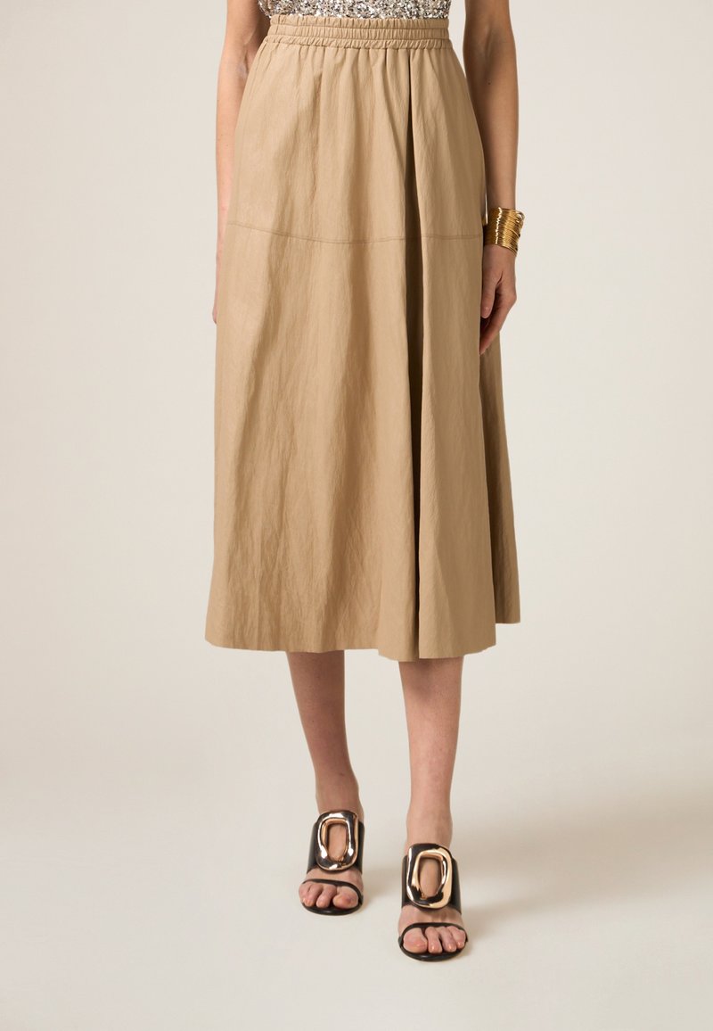 Beige, middellange rok met een elastische tailleband, met een zachte, gekreukte textuur. Gepaard met zwarte slidesandalen versierd met gouden hardware accenten.