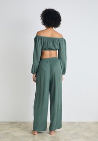 Zeleni crop top brez naramnic z dolgimi rokavi, v kombinaciji z ohlapnimi širokimi hlačami. Mehka tkanina in tekoča tekstura. Minimalističen dizajn.
