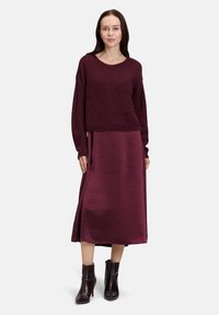 Femme portant un pull en tricot bordeaux associé à une jupe midi en satin assortie et des bottines en cuir brun foncé.