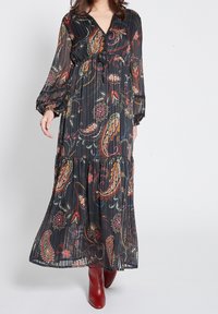 Musta kukkakuosis maxi-mekko, jossa on pitkät puffihihat, V-aukko ja vyötäröllä oleva vyö. Mekossa on värikkäitä paisley- ja kukkakuoseja läpikuultavalla kankaalla.