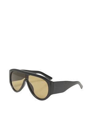 Lunettes de soleil enveloppantes noires avec de larges branches et des verres teintés jaune, inclinées pour montrer les détails de face et de côté.