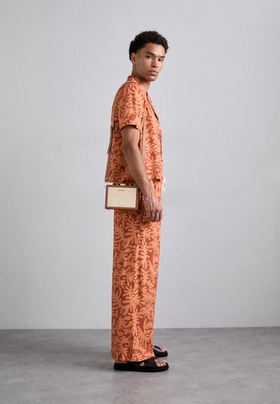 Orange patterned short-sleeve shirt and wide-leg pants, paired with a beige and tan crossbody bag, and black slide sandals.