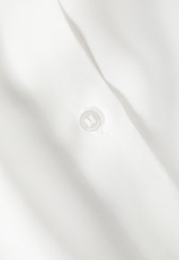 White fabric with a smooth texture and subtle sheen, featuring a round, clear button that has a logo embossed on it.
