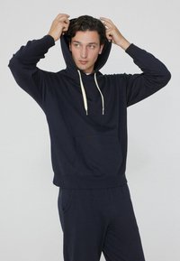 Navy Hoodie aus weichem Stoff, mit einer Fronttasche, Kordelzugverschluss und Rippbündchen. Teil eines passenden Jogger-Sets.