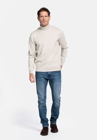 Licht beige coltrui in zachte brei, gecombineerd met blauwe jeans en bruine suède laarzen. Eenvoudig ontwerp zonder zichtbare patronen.