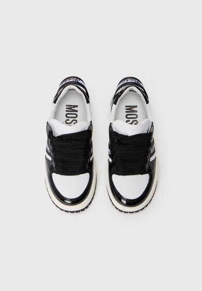 Black and white sneakers featuring a patent leather finish, textured black laces, padded collar, and contrasting white accents on the toe and sides.