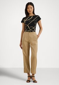 Juoda marškinėliai su gelsvu abstrakčiu raštu, derinami su aukštakulniais gelsvais kelnėmis su apsiūtais galais ir juodomis aukštakulnėmis sandalais.