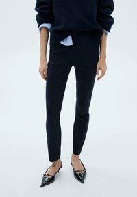 Tmavě modré slim-fit kalhoty vyrobené z hladké látky, s vysokým pasem a zúženým střihem, doplněné černými lodičkami se špičatou špičkou.