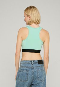 Mintgrøn crop top med en sort kant i bunden, der har racerback-design og en glat tekstur, parret med højhalsede jeans i denim.