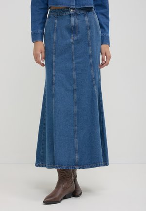 Langer blauer Jeansrock mit vertikalen Nähten, getragen mit braunen Leder-Cowboy-Stiefeln und einer passenden Jeansjacke.