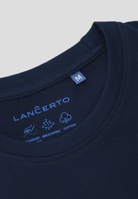 Granatowa bawełniana koszulka z okrągłym dekoltem, z niebieską metką oznaczoną literą "M" oraz nadrukowanymi ikonami przedstawiającymi przyjemny i oddychający materiał.