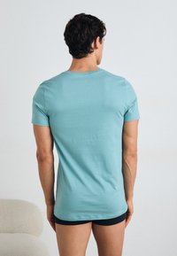 Light blue cotton t-shirt with short sleeves, round neckline, and a smooth texture, viewed from the back. Black shorts visible at the bottom.