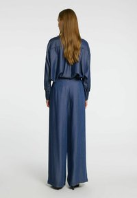 Denimoutfit med en löst sittande långärmad skjorta och vida byxor i en mörkblå nyans, med mjuk textur och subtil lyster.