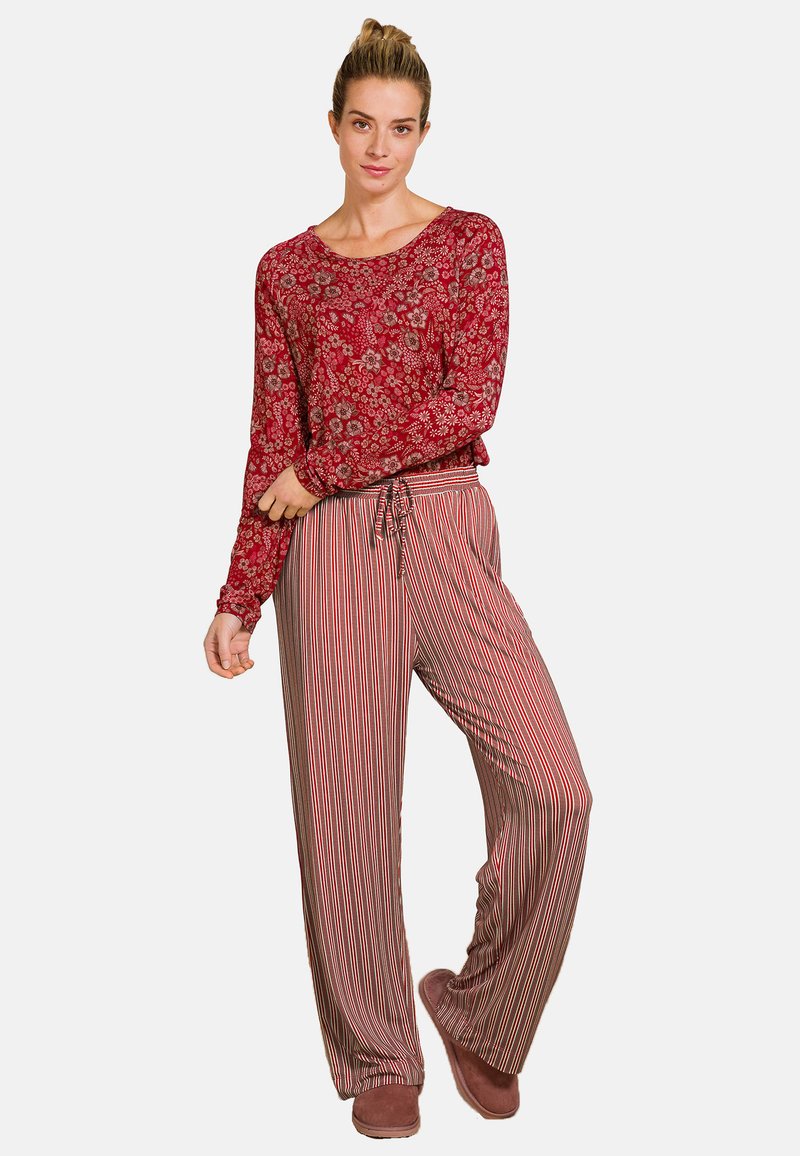 Langemouwen rode bloemen top gecombineerd met gestreepte, wijde broek. Beide gemaakt van zachte stof. De outfit wordt aangevuld met bruine slippers.