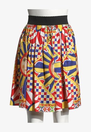 Jupe avec taille élastique noire présentant des motifs lumineux multicolores de visages de soleil et des formes géométriques rouges, bleues, jaunes sur tissu blanc.