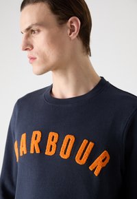 Sweatshirt azul marinho com um logo texturizado laranja "BARBOUR" no peito. Design clássico de gola redonda com punhos e bainha canelados.