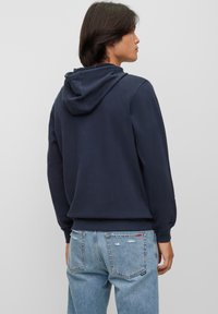 Navy blå hettegenser med snor, myk stoff og ribbestrikkede mansjetter. Båret med lyseblå slitte jeans. Enkel, ren design.