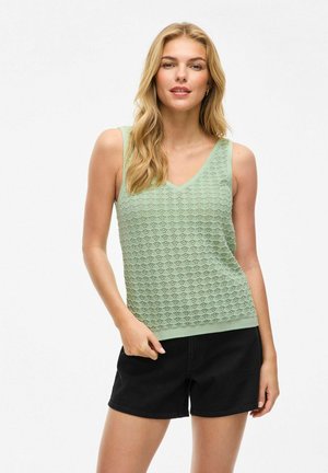 Haut sans manches vert clair avec un décolleté en V, présentant un motif en losanges texturé, associé à un short noir.