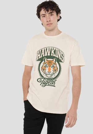 Cream cotton t-shirt featuring a large tiger graphic with orange and black details, surrounded by text "HAWKINS" and "Tigers" in green.