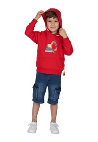 Felpa rossa con una grafica di un veicolo da costruzione, abbinata a pantaloni cargo blu navy e sneakers bianche. La felpa ha un cappuccio con lacci.