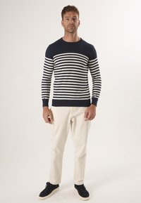 Marineblauwe en crèmekleurige gestreepte trui met een ronde halslijn, lange mouwen en ribgebreide manchetten, gecombineerd met lichtbeige broek en zwarte sneakers.