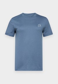 Camiseta de manga corta con cuello redondo en algodón azul moderado, con un sutil logo "Ck" bordado en el lado izquierdo del pecho. Textura suave, diseño minimalista.