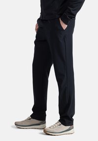 Schwarze Sporthosen mit glatter Textur, ausgestattet mit Seitentaschen und einem schmal zulaufenden Design. Getragen mit hellen Laufschuhen.