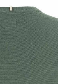 Gros plan sur un tissu tricoté gris-vert avec un petit détail en boucle rayée beige et noire près de la couture.