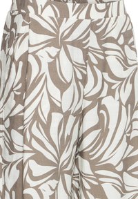 Smėlio ir baltos spalvos tropinių lapų raštuota medžiaga su klostėmis, dalis drabužio juosmens ir viršutinės dalies.