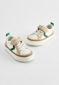 Hvide lædersneakers og beige suedettes med grønne accenter, snørebånd og Velcro-strop, med en struktureret gummisål og glat overdel.