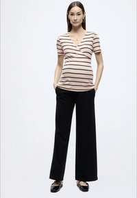 Τοπ εγκυμοσύνης με κοντά μανίκια σε ανοιχτό ροζ και σκούρες καφέ ρίγες, σε συνδυασμό με φαρδιά μαύρη παντελόνα και μαύρες μπαλαρίνες.