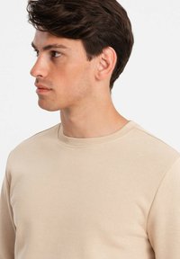 Beige Baumwollpullover mit geripptem Rundhalsausschnitt und glatter Textur. Verfügt über eine figurbetonte Passform und lange Ärmel.