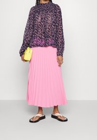Gennemsigtig navy bluse med pink blomsterprint, plisseret pink midi-nederdel og to-farvede sandaler. Outfittet inkluderer en lille gul håndtaske.