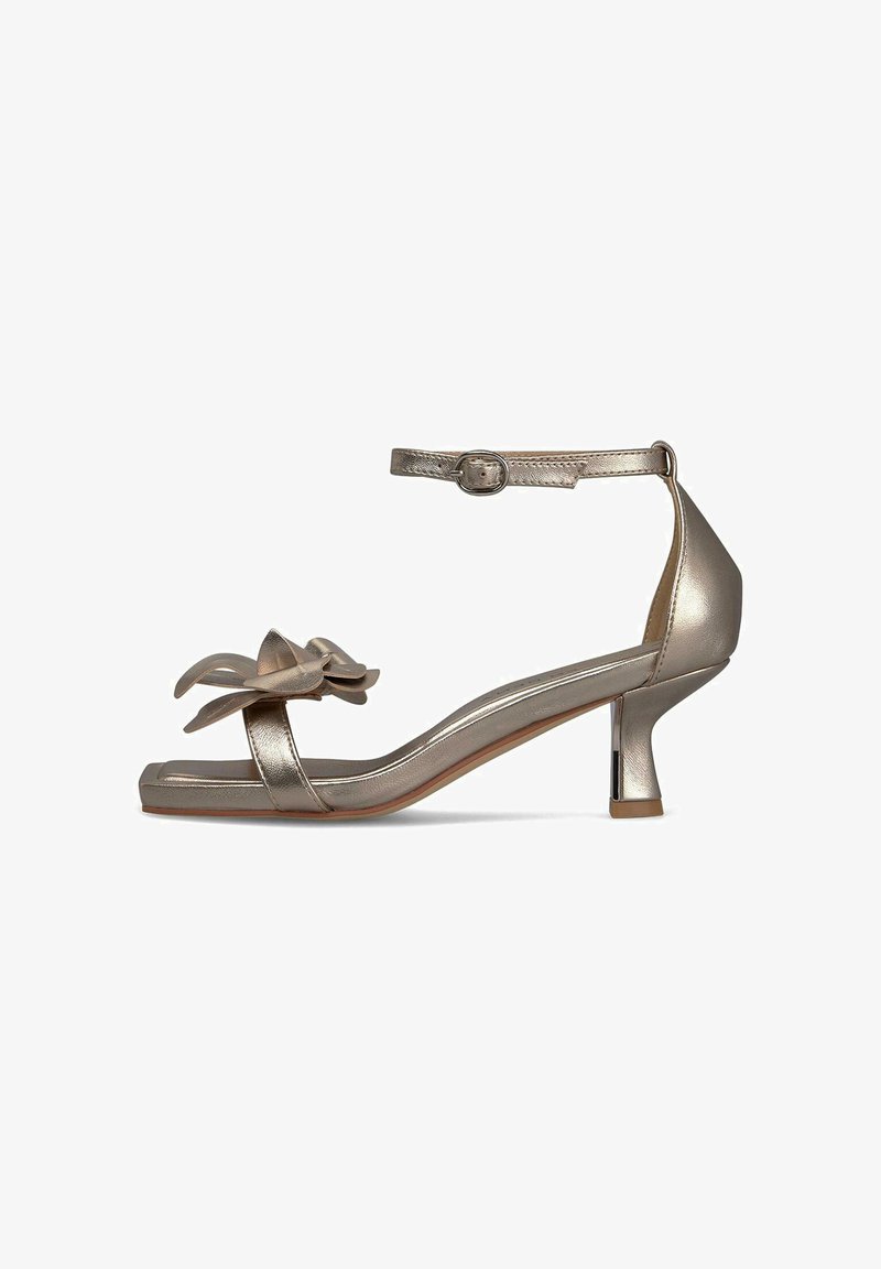 Metallisch gouden hoge hakken sandaal met een verstelbaar enkelbandje, open teen en een bloemenaccent op de wreef. Vierkante teen ontwerp.
