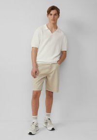Korte mouw, wit textuur polo met V-hals, gecombineerd met beige shorts en lichte sneakers met grijze accenten.
