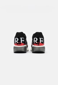 Paire de baskets noires en mesh avec semelles épaisses grises et accents rouges, affichant le nom de la marque "REPLAY" en grandes lettres blanches à l'arrière.
